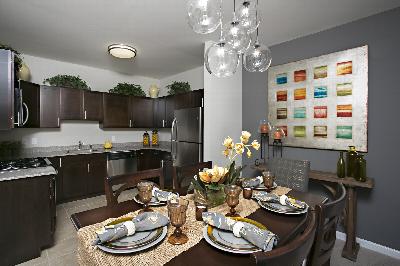Autumn Hills kitchen photo shows dark cabinets, granite countertops and stainless steel appliances. In the foreground there is a table for 6 with place settings out. A large piece of wall art hangs near the dining area, and other decorations are shown.