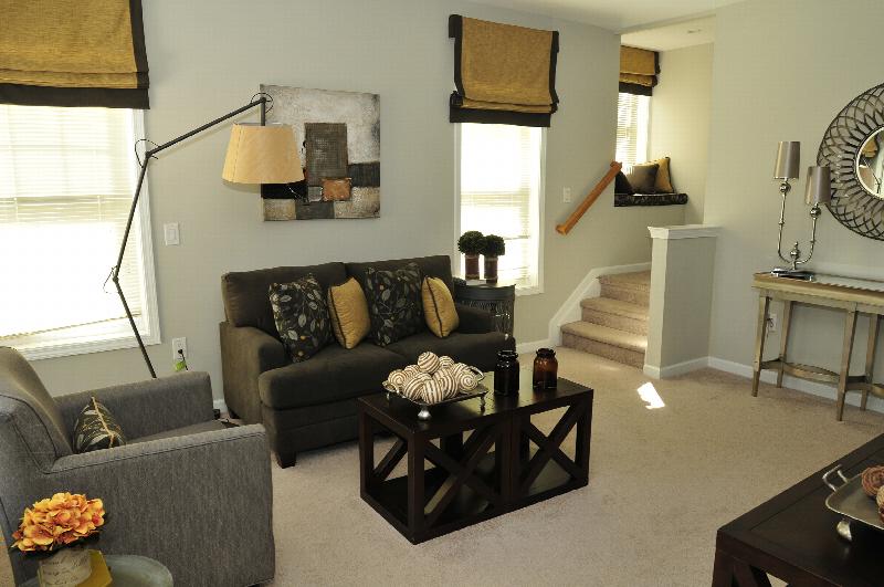 Autumn Hills Living Room photo shows a seating area, coffee table and stairs leading up to another room. Window treatments, throw pillows and other items decorate the room.
