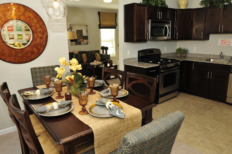 Autumn Hills dining room photo features a table for 6 with place settings out. A large piece of wall art hangs near the dining area, and other decorations are shown. The kitchen area can be seen off to the right.