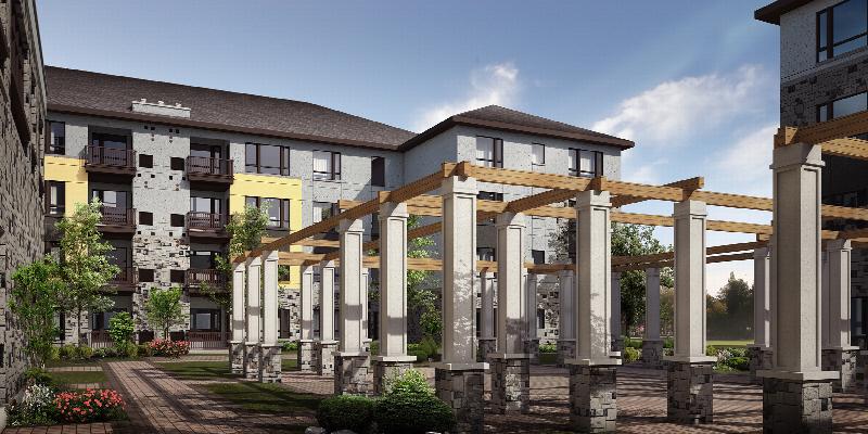 Next at Xchange exterior photo shows spacious community courtyard with large pergola. Garden style shrubs, green grass and trees highlight the surrounding landscaping. A four story apartment building with light colored brick and stone facade can be seen in the background.