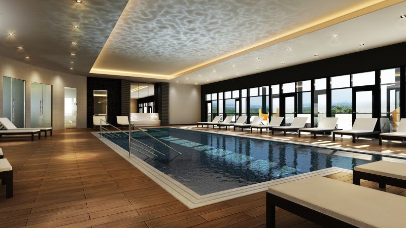 Next at Xchange photo shows state of the art indoor pool and sauna. Modern lounge chairs surround the lit indoor pool area. Large folding doors leading to the outdoor deck area can be seen in the background.