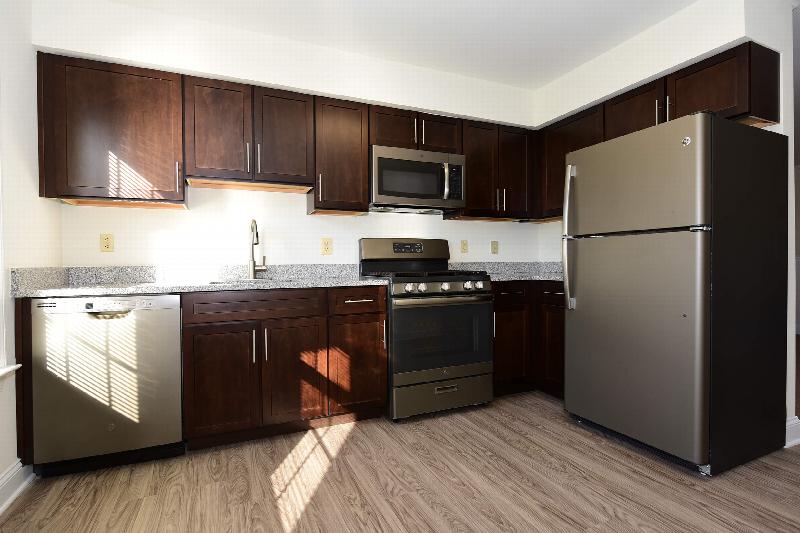 Pike Run Village interior photo of the renovated kitchen showing new kitchen cabinets and hardware, granite countertops, stainless steel appliances and wood grain tile flooring.