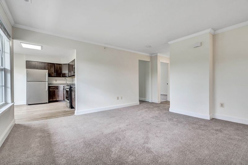 Interior photo of a renovated apartment at Pike Run Village, showing a living room with new carpet and paint. Entry to the kitchen is shown.