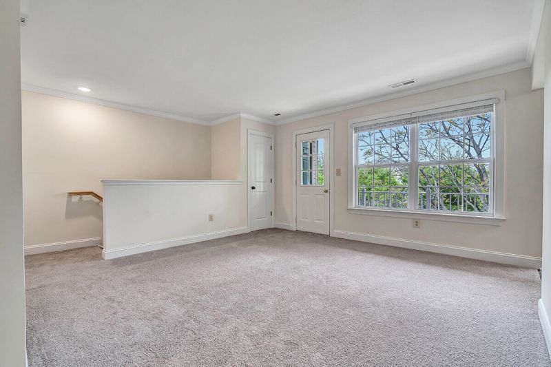 Interior photo of a renovated apartment at Pike Run Village, showing a living room with several windows allowing natural light. There is new wall to wall carpeting and fresh paint.