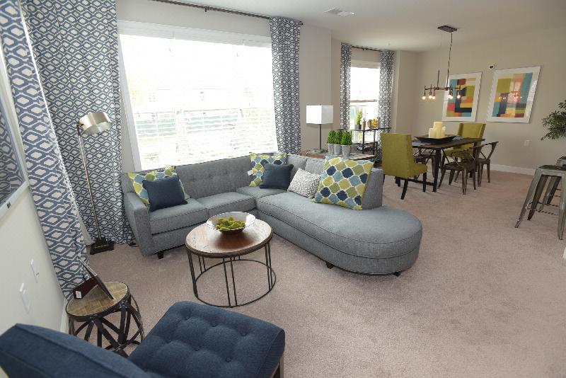 Woodhaven Commons living room features a seating area with large window letting in natural light. The dining room area can be seen in the distance.