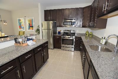 Woodhaven Commons kitchen shows dark cabinets with granite countertops and stainless steel appliances. Several decorations are displayed on the counters.