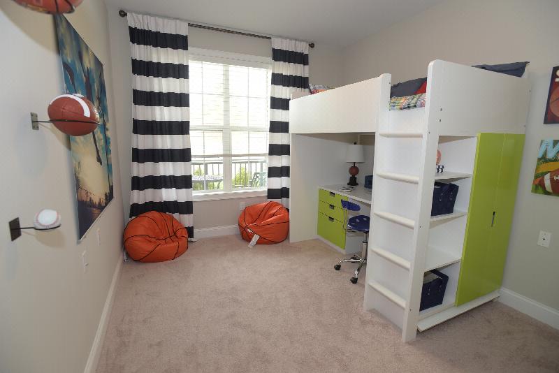 Woodhaven Commons kids bedroom photo shows a bed above with a desk below. A large window lets in natural light. The room is decorated with a sports theme.