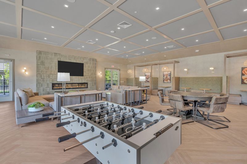 Interior photo of the community room inside the clubhouse at Woodhaven, featuring laminate wood flooring, several seating areas for congregating, a large fireplace with TV above, and several games such as foosball and a poker table.