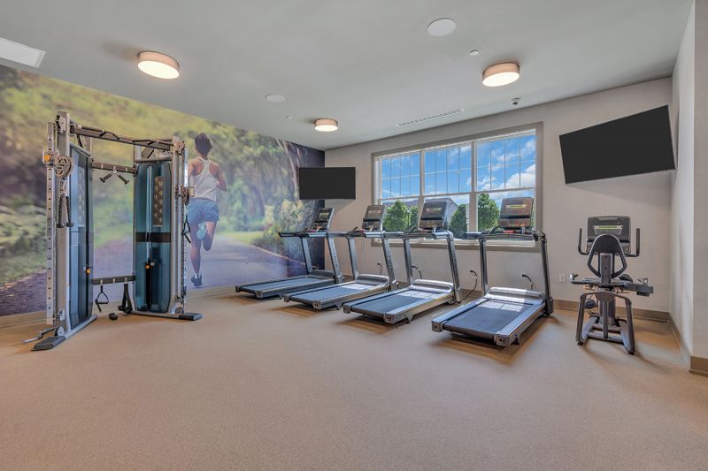 Interior photo of the gym inside the clubhouse at Woodhaven, showing a resistance training machine, several treadmills and a stationary bike.