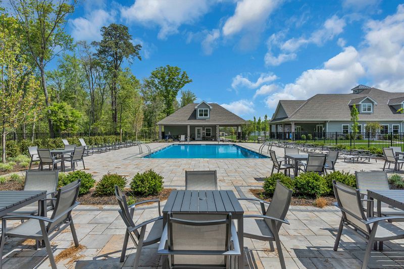 Exterior photo of the poll at the clubhouse at Woodhaven, showing a large swimming pool surrounded by ample seating and a pool house.
