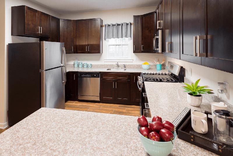 Gardens at Jackson Twenty One Interior photo showing espresso cabinets, stainless steel appliances and laminate flooring. There are decorations on the kitchen counter and a window to allow natural light to enter the room.