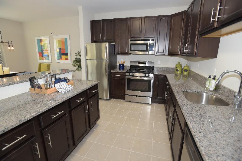 Woodhaven Commons kitchen shows dark cabinets with granite countertops and stainless steel appliances. Several decorations are displayed on the counters.