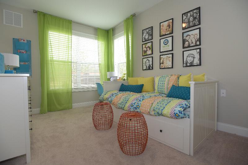 Woodhaven Commons bedroom image shows a daybed and dresser, artwork on the walls, and bright green window treatments on the windows.