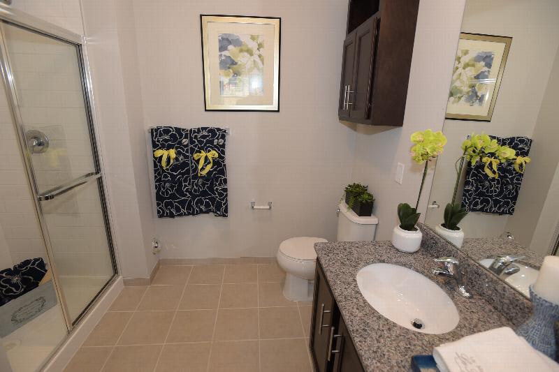 Woodhaven Commons bathroom photo shows a shower stall, a vanity with granite countertops and a mirror above. There is a toilet with medicine cabinet above.