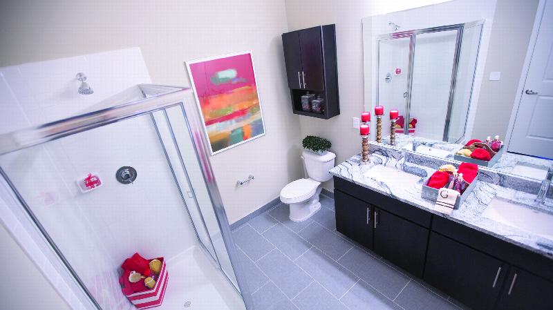The Grove at One92 Bathroom photo showing a dual sink espresso vanity with a granite counter top and a mirror on the wall, a stand up shower and a toilet. There are decorations on the counter top and on the walls.