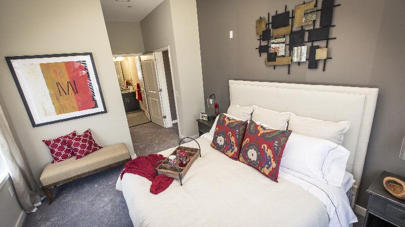 The Grove at One92 Bedroom showing a queen sized bed, two nightstands with lamps, and a bench against the wall. There are decorations on the nightstands and the bed. The bathroom can be seen in the background.