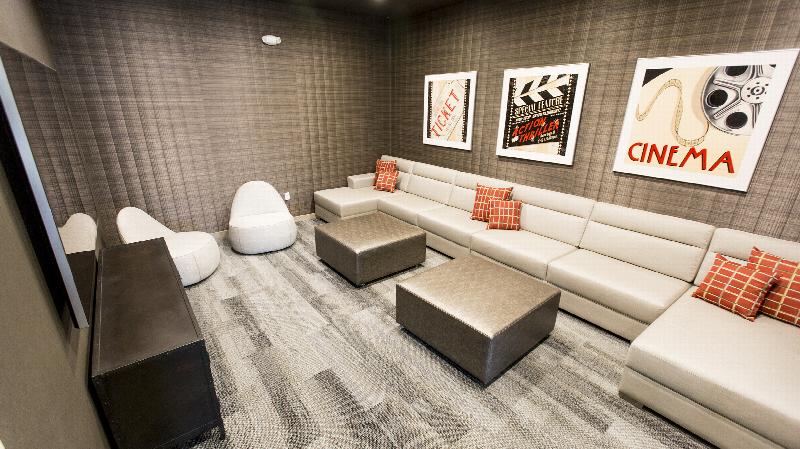 The Grove at One92 Lounge photo showing a large sectional couch with two ottomans and two chairs. There is an entertainment center with a T.V. on the wall. There are movie pictures on the wall behind the couch.