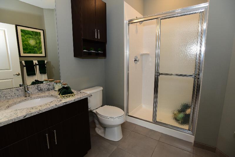 Station Village at Avenel bathroom image shows a shower stall with sliding shower doors, a toilet, a vanity with granite countertops and a mirror above the sink.