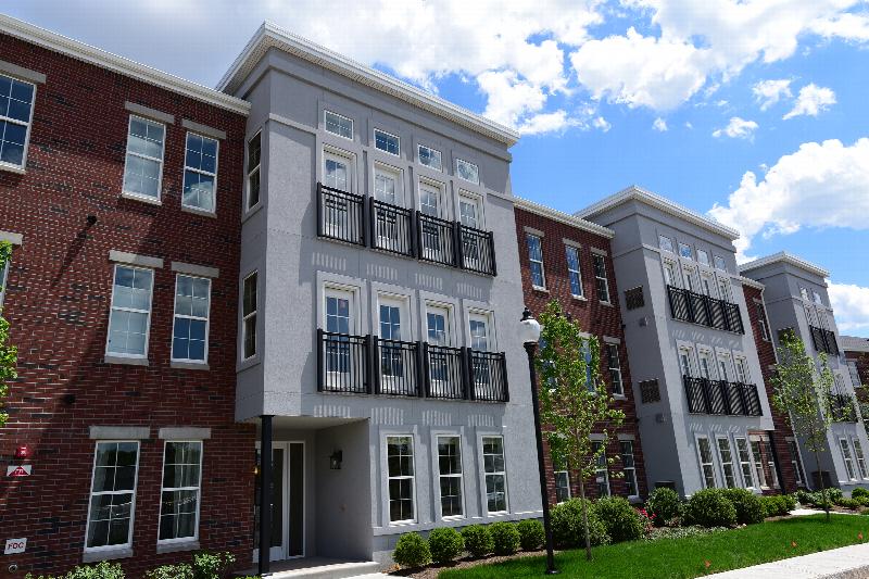 Station Village Affordable Exterior photo showing a dark reddish brick and gray stucco exterior. and a street light. Several bushes and trees highlight the landscape.