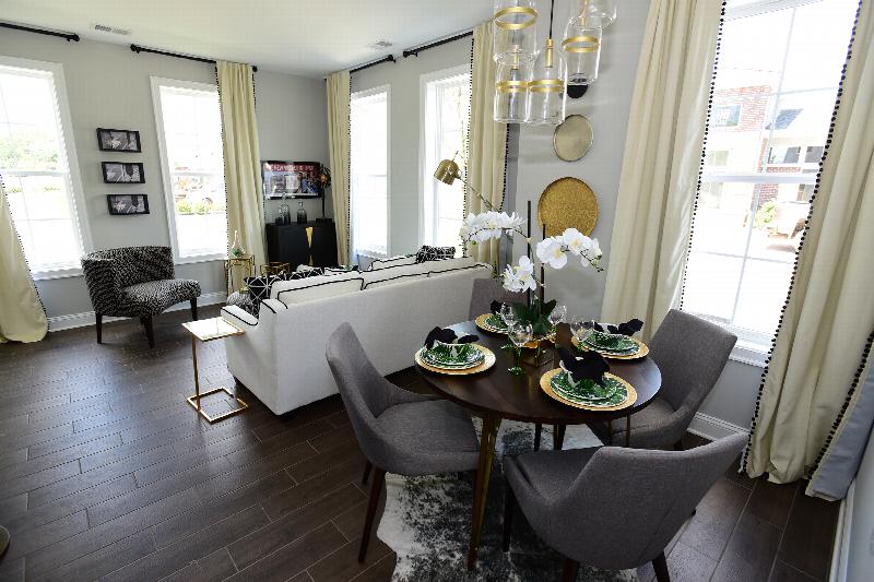 Station Village Affordable Interior photo showing a round table with four chairs, a couch and a chair. There are decorations on the table and on the walls. There are several large windows which allow natural light to enter the room.