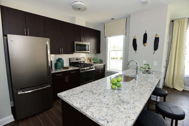 Station Village Affordable Kitchen photo showing espresso cabinets, granite counter tops and stainless steel appliances. Laminate flooring runs throughout the apartment. There are decorations on the counter top and on the walls.