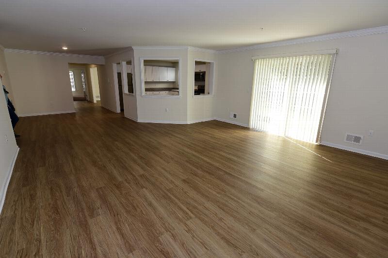 Pike Run Meadows interior photo showing a renovated apartment with wood grain flooring, a sliding glass door to a balcony. You can see the kitchen in the background and a hallway leading to additional rooms
