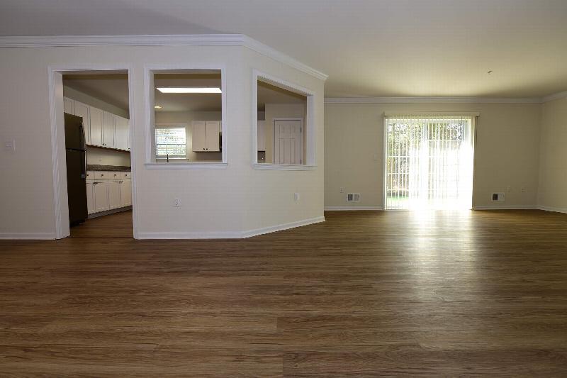 Pike Run Meadows interior photo showing a renovated apartment with wood grain flooring, a sliding glass door to a balcony. You can see the kitchen in the background.