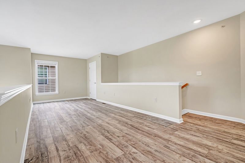 Interior photo of a renovated apartment at Pike Run Meadows, showing the second floor with woodgrain flooring and new paint. Stairs back to the first level are shown on the right.